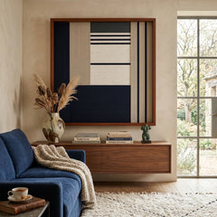 Beautiful framed hand-woven textile wall art styled elegantly above a floating wooden credenza behind a plush blue sofa in a sunlit living room.