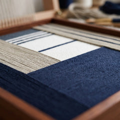 Extreme low-angle macro shot of the Baltic Window hand-woven textile art lying flat, highlighting the textured deep navy blue patch over white and beige yarn stripes.