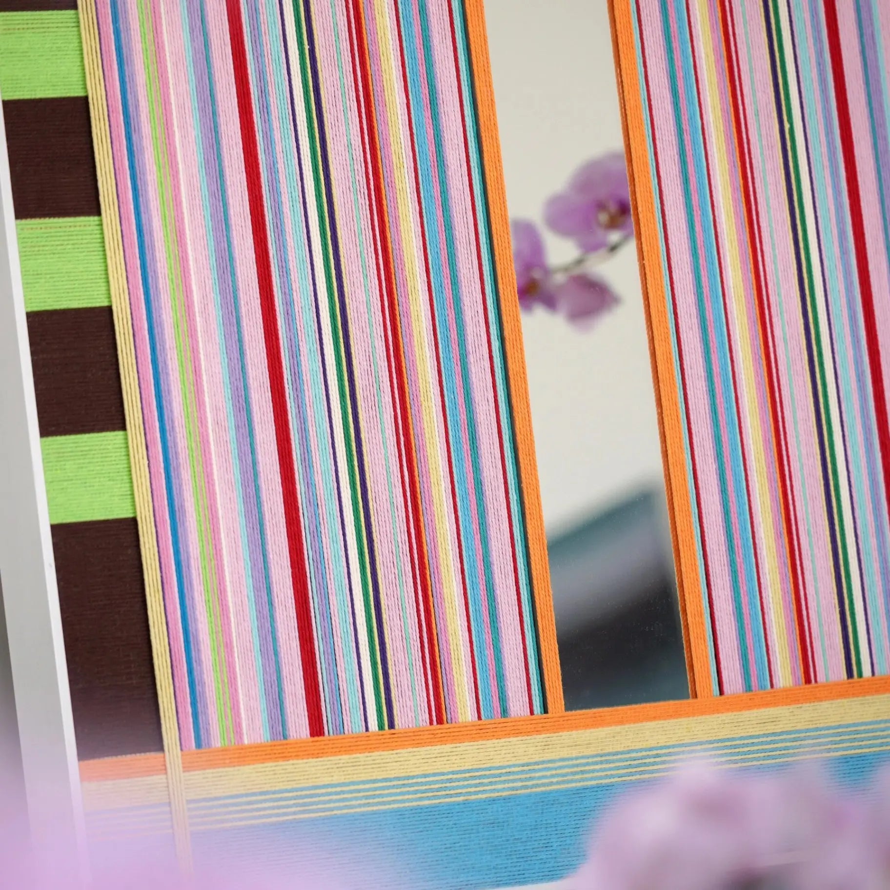 Blooming Flowers wool yarn art resting on an outdoor stone bench, highlighting its delicate pastel stripes against a natural stone backdrop.