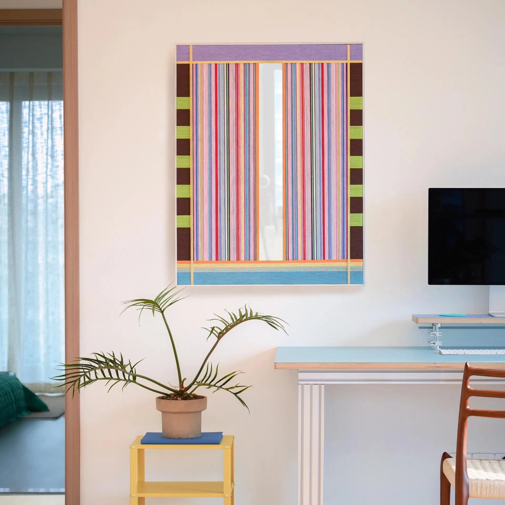 Blooming Flowers yarn wall art styled on a desk next to a lamp and notebook, showcasing its vibrant spring-inspired stripe palette and precise stitch alignment.