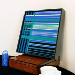 Blues Harmony yarn woven art styled on a desk next to a soda can and glass, highlighting its precise stripe alignment and modern frame