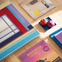 Bohemian Reverie yarn mirror art resting on a desk beside a yellow ball and cup, emphasizing its compact square form and bold frame.