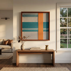 Square teal and orange textured woven art creating a vibrant focal point in a bright, modern hallway above a simple wooden bench.
