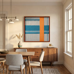 Breeze of Capri hand-woven textile art hanging above a dark wood credenza in a contemporary dining room with a wooden table and grey chairs.