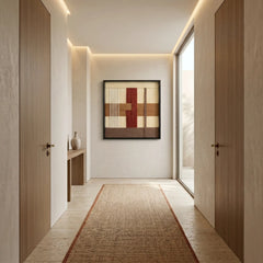Large square hand-woven wool wall art in sunset tones hanging as a focal point at the end of a modern minimalist hallway with a jute runner rug.