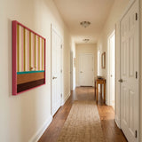 Angled perspective of the Coral Stripe Pup Wander textile wall art hanging on a white wall in a long, well-lit hallway corridor.
