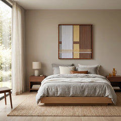 Large-scale textured fiber wall art hanging above a platform bed with grey linens in a peaceful, minimalist bedroom with natural lighting.