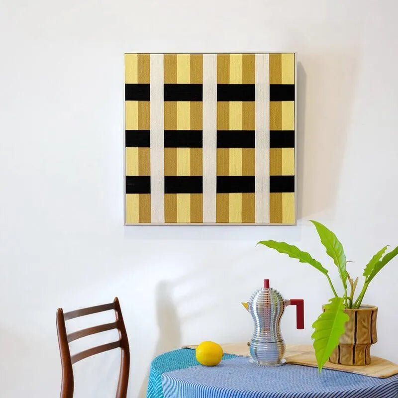 Downton Manor yarn wall art leaning on a chair in sunlight, showcasing its bold grid pattern and sturdy frame.
