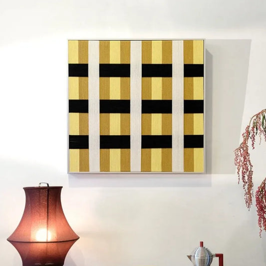 Downton Manor hand-woven yarn wall art in alternating black and gold grid panels, framed in natural wood and displayed above a console table.