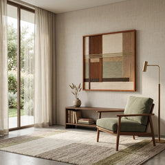 Square hand-woven textile art piece shown in a bright living space next to a green armchair and large window with natural light.