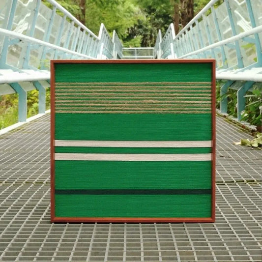 Endless Flow hand-woven wool yarn wall art featuring alternating deep and mint green vertical stripes in a natural wood frame, showcased outdoors