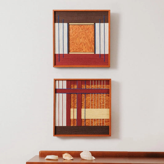 Two framed "Festive Harmony" hand-woven wool art pieces hanging vertically above a wooden console, featuring warm orange and blue geometric patterns.