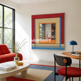 Fields of Blossoms red, blue, cream, and orange yarn-framed mirror displayed in a colorful sunlit reading room.