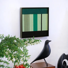 Hand-held view showing the compact square form of Green Branches yarn wall art, with precise stripe alignment and a sturdy black frame.
