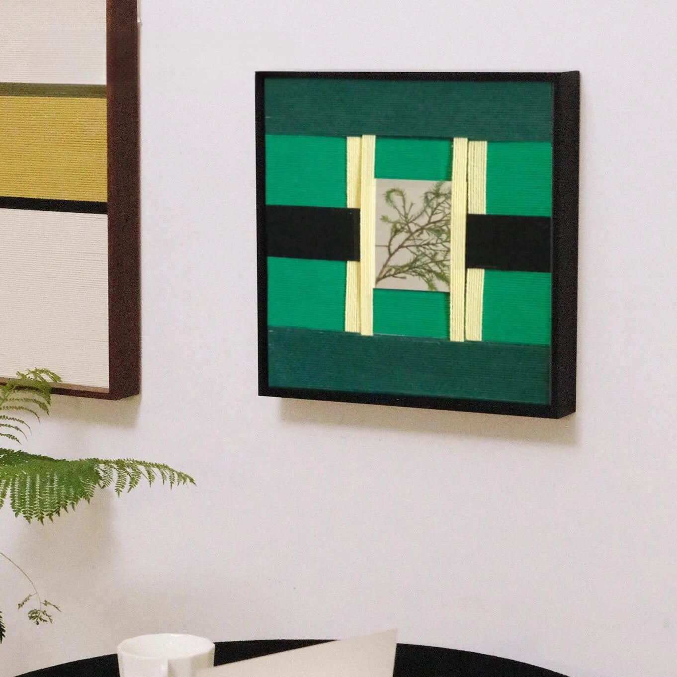 Green Glow yarn wall art mounted on a white wall above a small chair, highlighting its bold green stripe design and botanical center