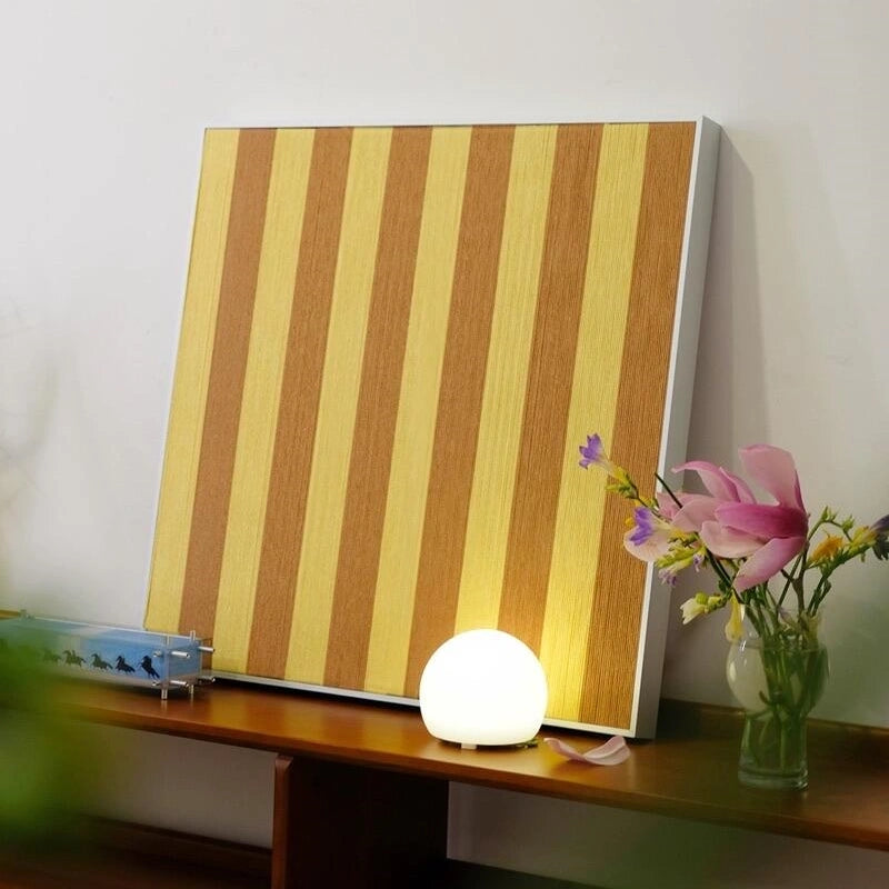 Angled view of Hana & Alice yellow stripe art leaning on a tabletop next to decorative objects, highlighting its geometric pattern and color contrast