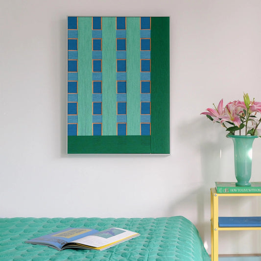 Large vertical hand-woven wool wall art featuring green and blue geometric stripes, styled in a colorful bedroom with a teal quilt and yellow side table.