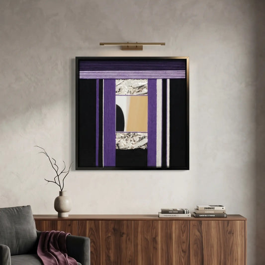 Square hand-woven wool wall art in a black frame featuring an abstract composition of deep purple, black, and gold geometric panels, illuminated by a brass picture light above a walnut sideboard.