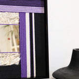 Angled view of HOUTIAN yarn mirror art leaning on a tabletop, highlighting the contrast between purple yarn stripes and black frame with integrated mirror.