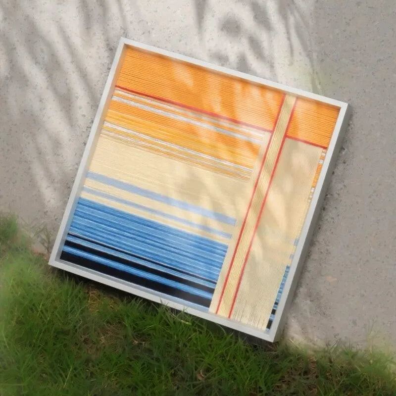 Love at Sunset yarn woven wall art leaning outdoors against a concrete wall with grass background.