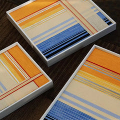 Close-up view of multiple hand-woven wool art pieces showing the intricate striped texture and high-quality white frames from an angled perspective.