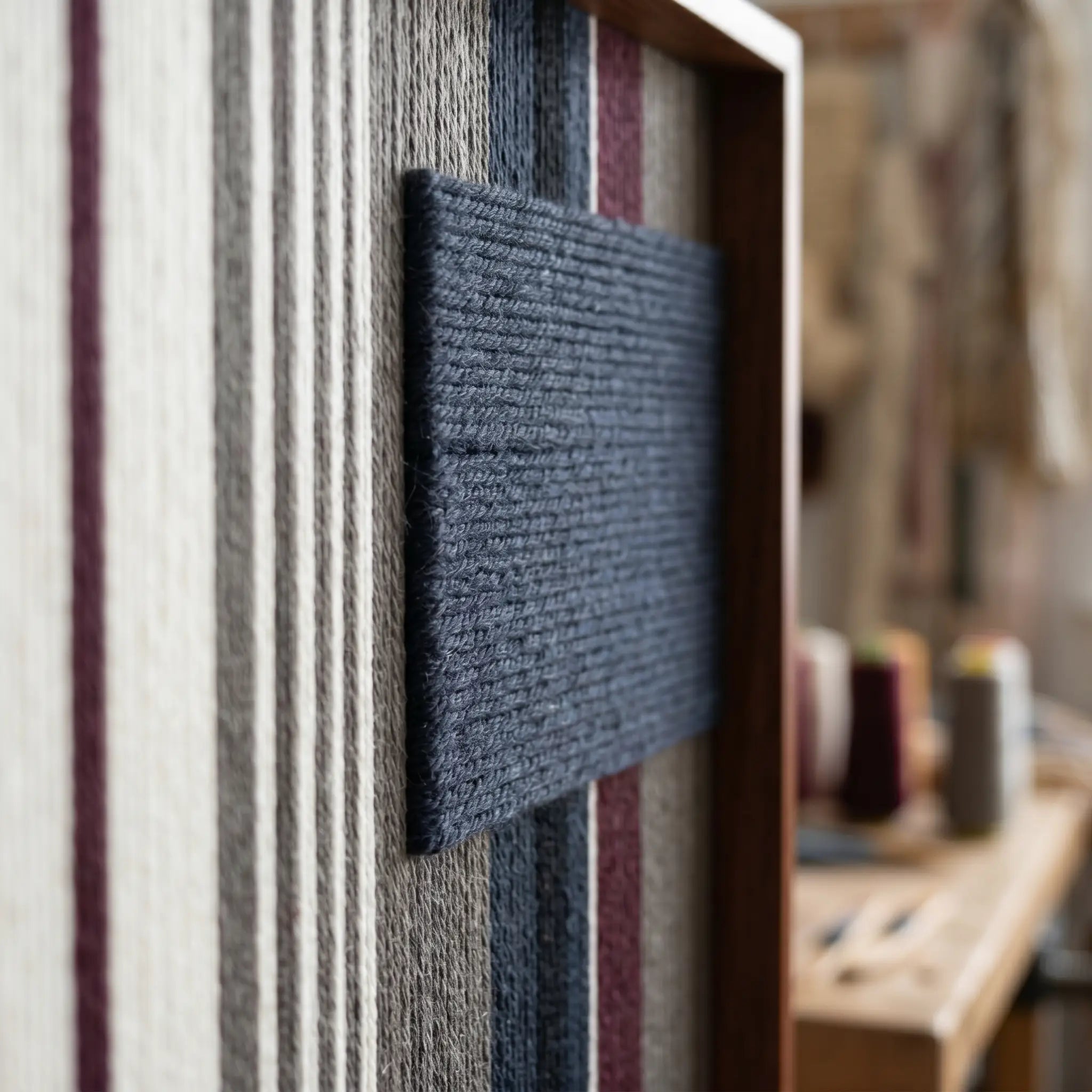 Angled close-up of the framed Midnight Fjord hand-woven tapestry showcasing the wooden frame and dimensional dark navy patch against striped wool.
