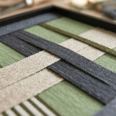 Macro shot of the Misty Forest hand-woven wool art highlighting the interlocking sage green, charcoal grey, and beige hand-wrapped yarn patterns.