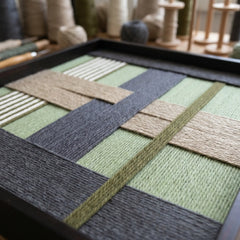 An angled perspective of the textured fiber wall art in a studio setting, showcasing the dimensional depth of the structural yarn layering.