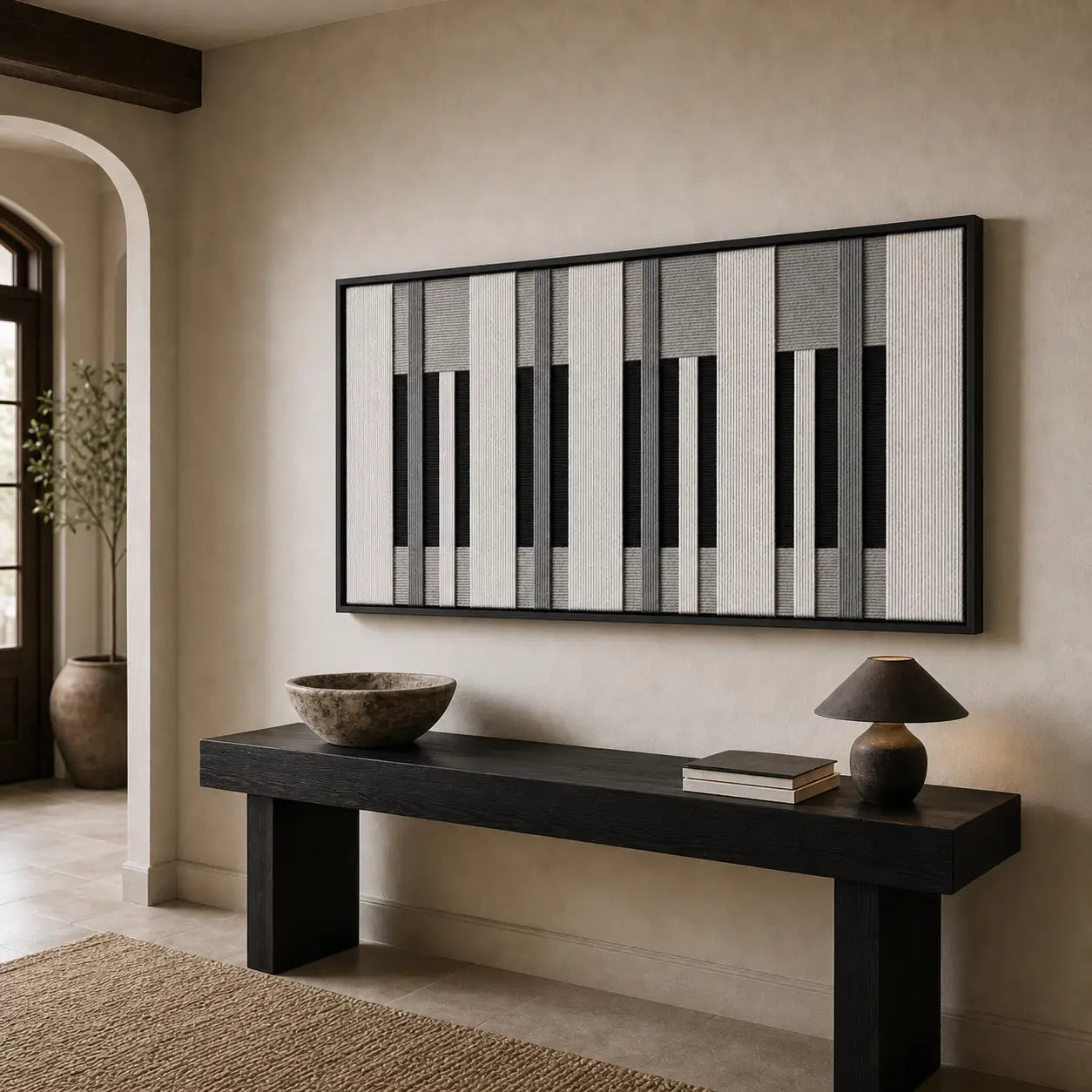 Striking monochrome hand-woven wool tapestry positioned perfectly above a sleek black console table in a bright, modern entryway hallway.