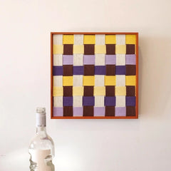 Front view of Mrs Dalloway yarn woven wall art mounted on wall next to a decorative bottle.