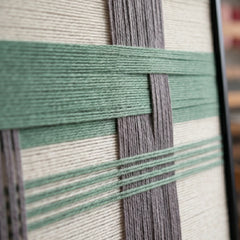 Macro close-up of the Muted Spring fiber art highlighting the structural layering of raised sage green yarn over vertical grey and cream background bands.