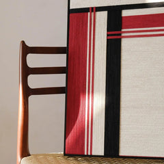 “Napoli” yarn woven wall art leaning on a chair, highlighting the sturdy dark wood frame and vibrant stripe composition