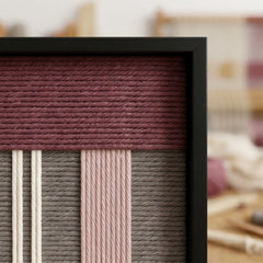 Angled close-up of the framed Nostalgic Bloom hand-woven tapestry showcasing the black frame and dimensional deep mauve, grey, and pink geometric wool patterns.