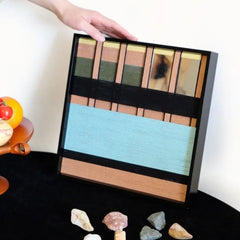 Hand-held view of Outside The Window yarn wall art showing its sturdy black frame and precise stitchwork of multicolored stripe panels.