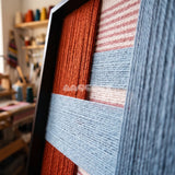 Detail of The Press Line framed textile wall art, featuring a two-piece geometric cotton cord composition in terracotta, sky blue, pink, and slate blue.