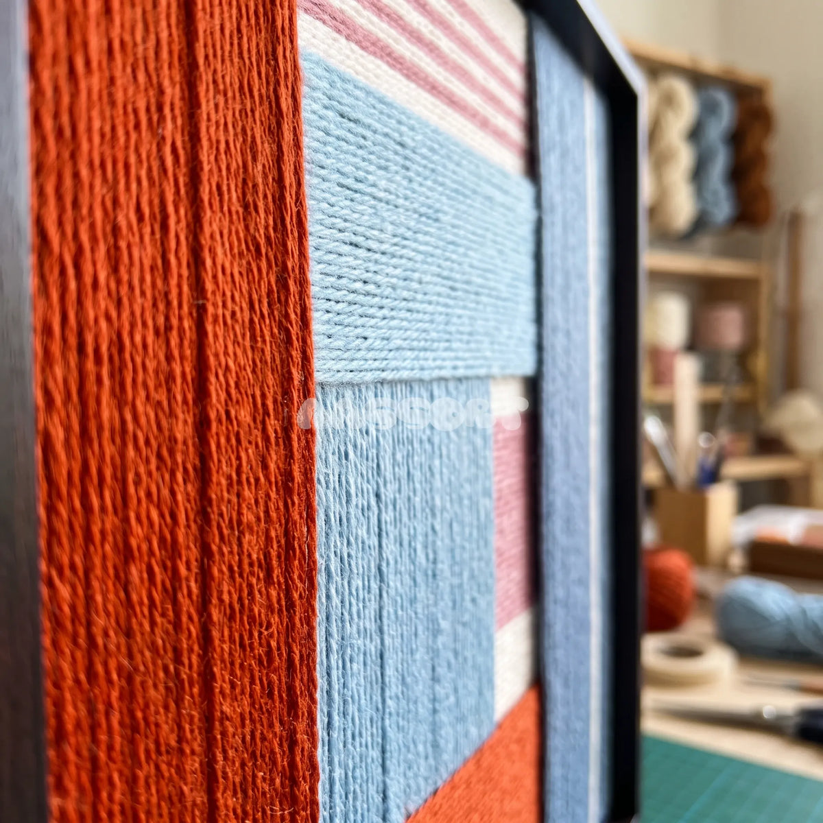 Detail of The Press Line framed textile wall art, featuring a two-piece geometric cotton cord composition in terracotta, sky blue, pink, and slate blue.