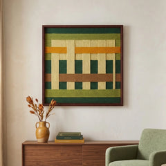 Framed fiber art tapestry with an earthy textured design displayed above a wooden sideboard next to a light green armchair.
