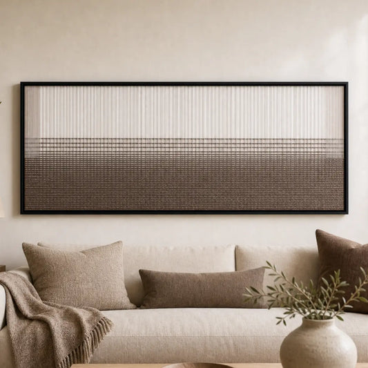 Large framed Quiet Thread hand-woven wall art hanging elegantly above a cozy cream sofa in a neutral living room.