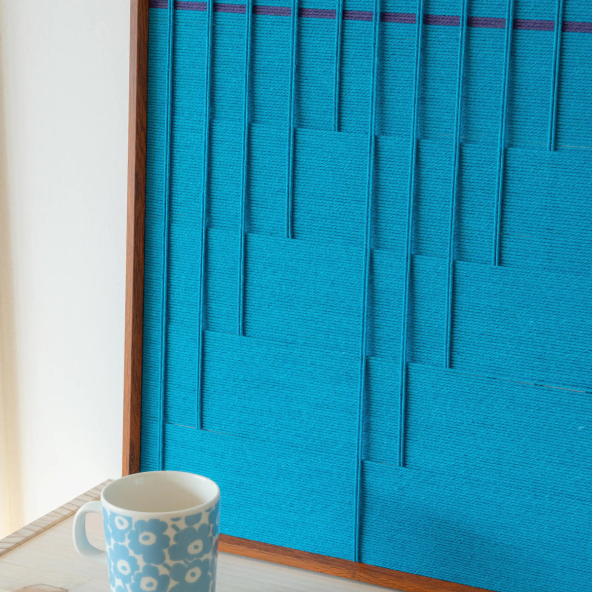 Close-up of Submersion RE018 textile art showing layered cerulean yarn, raised geometric lines, and its framed finish.