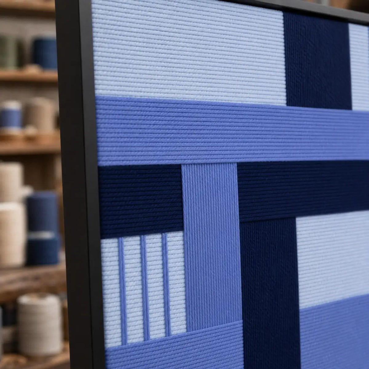 Angled close-up of Nordic Tide RE028 textile art showing its black frame and raised dimensional blue yarn texture.