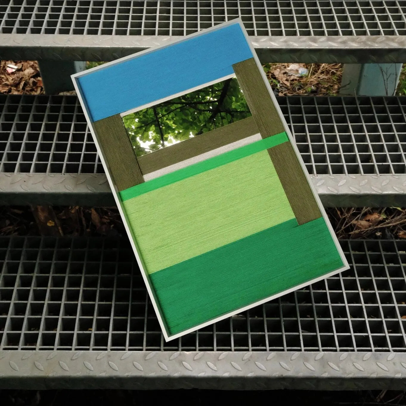 Riverside yarn wall art showcased on a metal grate, highlighting the crisp transitions between blue, grey, and green stripe panels