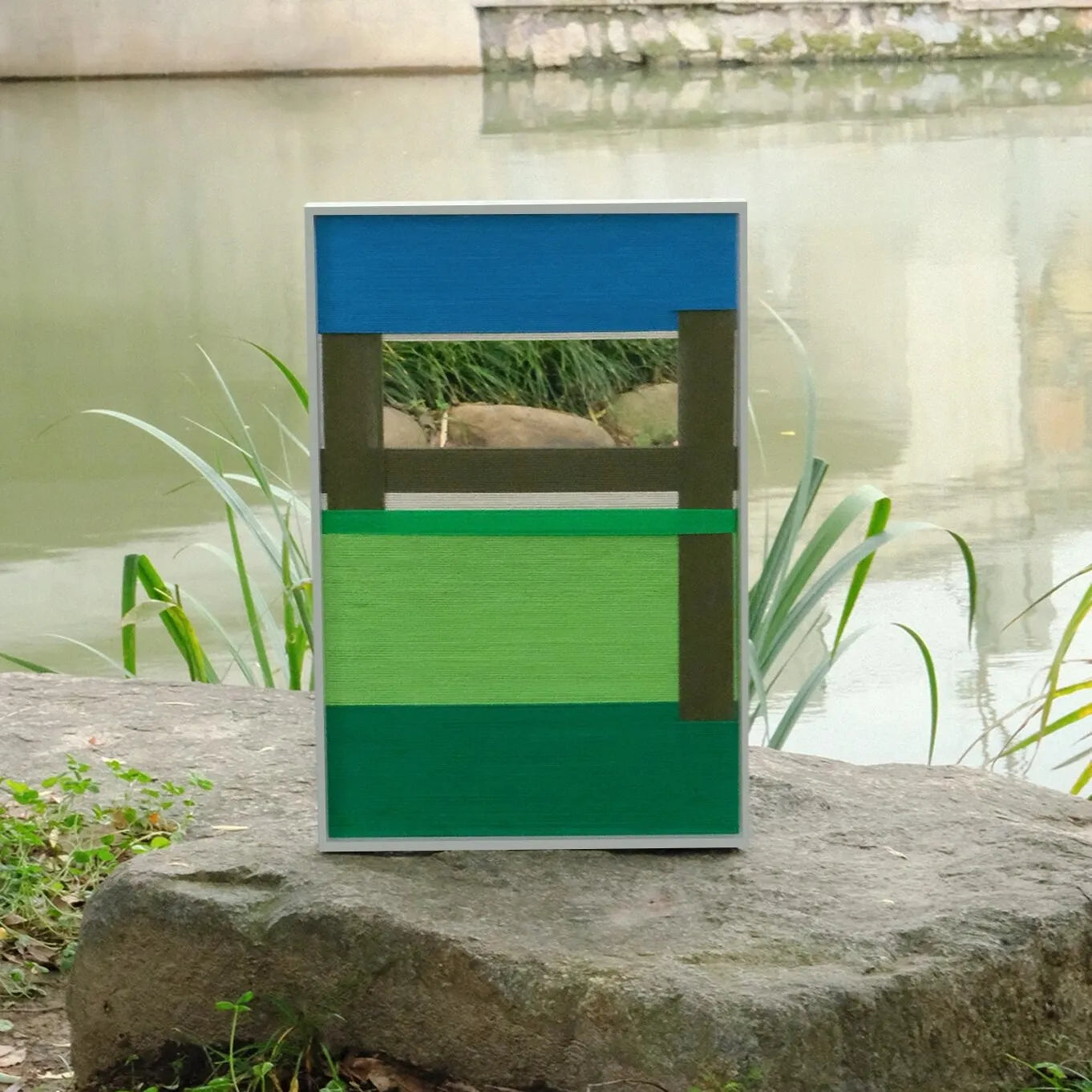 Riverside wool yarn wall art placed on a stone surface near moss, emphasizing its bold green accent stripe and tight weave texture