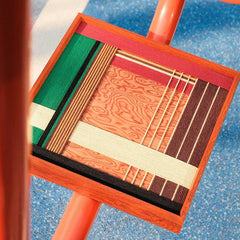 Saint Christmas yarn wall art leaning on a red metal railing, highlighting its vibrant red and green stripe pattern and precise weaving