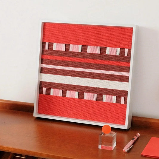 Spring Miss hand-woven yarn wall art in vibrant red, burgundy, and cream stripe panels with a minimalist white frame, displayed above a wooden console table.