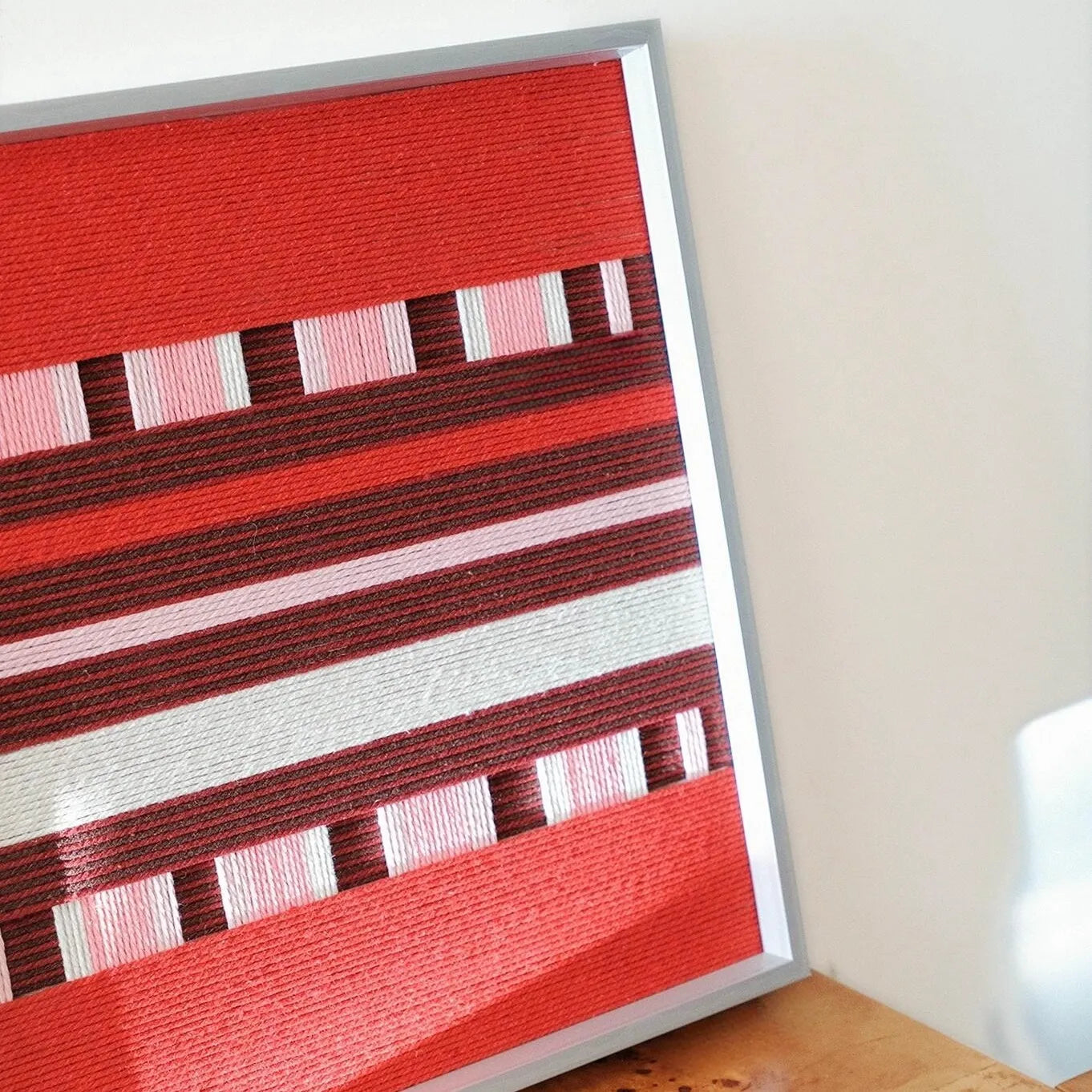 Spring Miss yarn wall art displayed at an angle on a desk beside a white block, showcasing clean stripe alignment and precise wooden frame.
