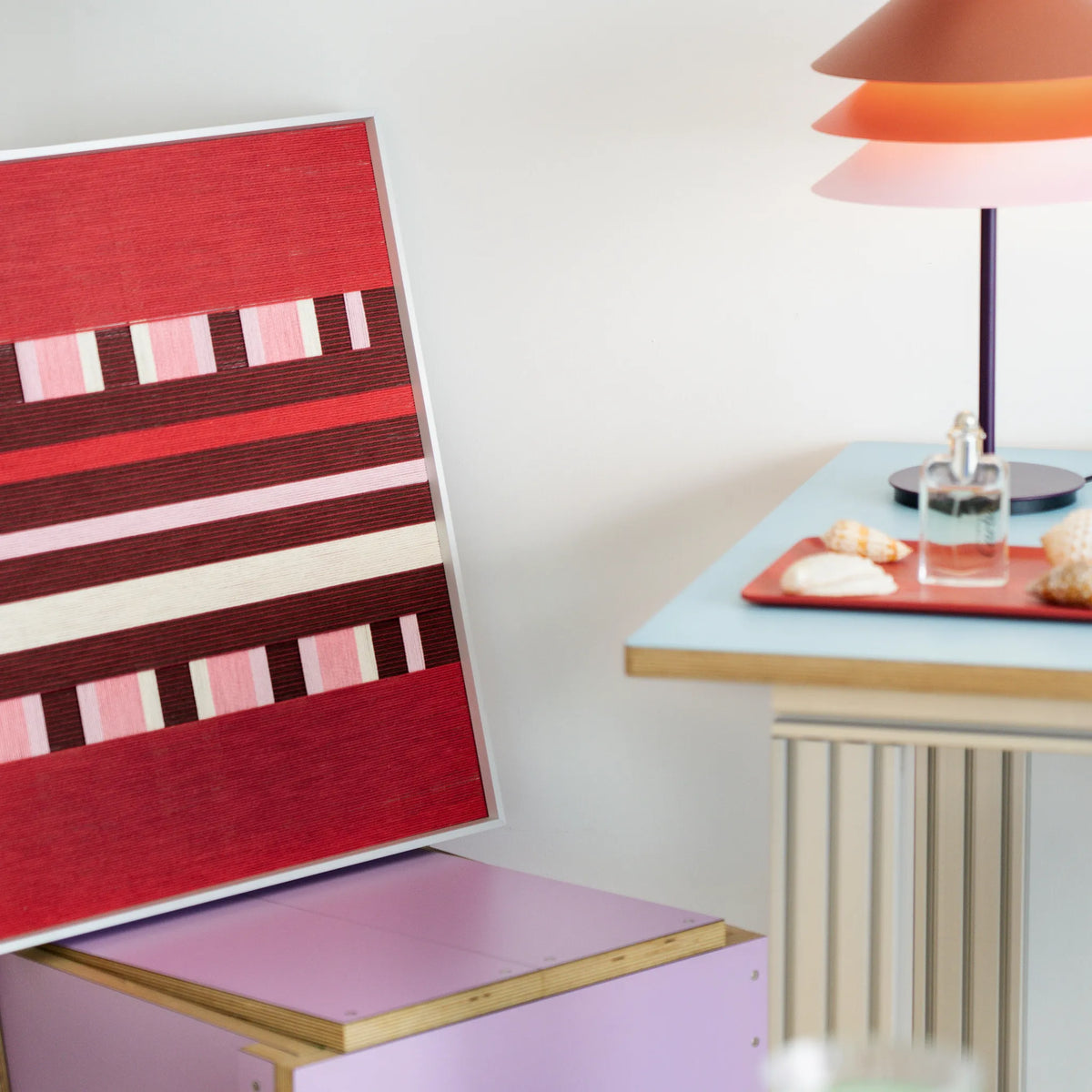 Spring Miss SQ029 red burgundy pink and cream framed yarn art leaning on a pastel shelf beside a table lamp