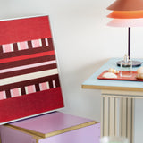 Spring Miss SQ029 red burgundy pink and cream framed yarn art leaning on a pastel shelf beside a table lamp