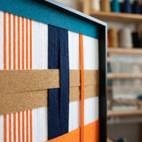 Side profile of Orange Midsummer SQ096 showing the sleek black frame and dimensional woven textile layers.