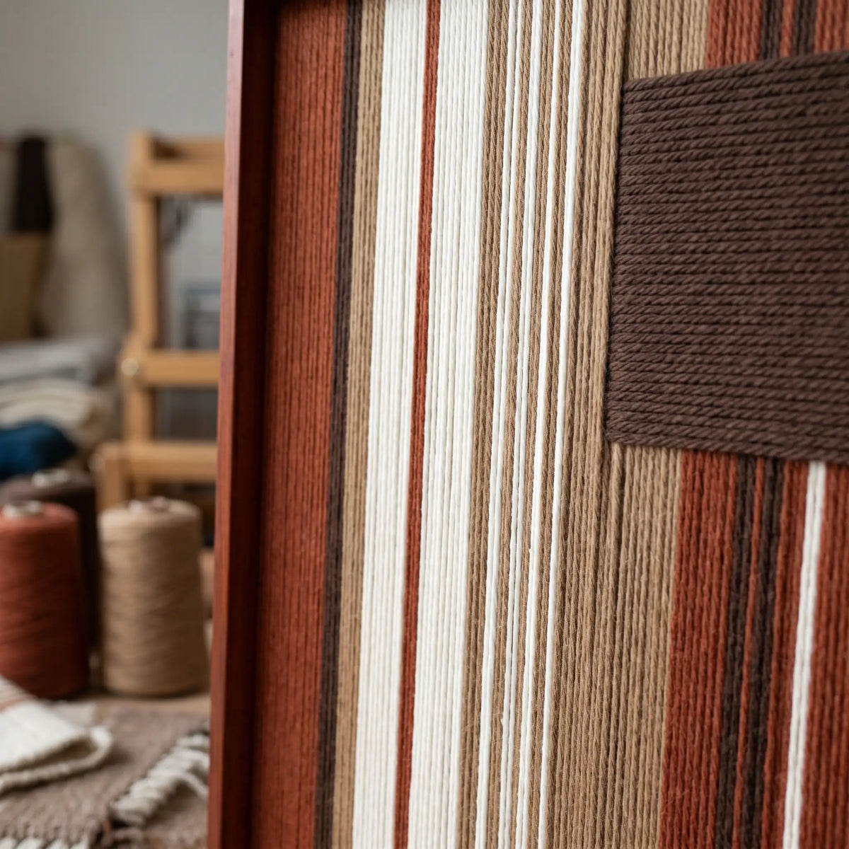 Angled close-up of Mocha Prelude SQ124 showing the frame and dimensional mocha block over earth-tone yarn stripes.