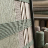 Angled close-up of Celadon Mist SQ137 showing the black frame and dimensional green and beige yarn patterns.